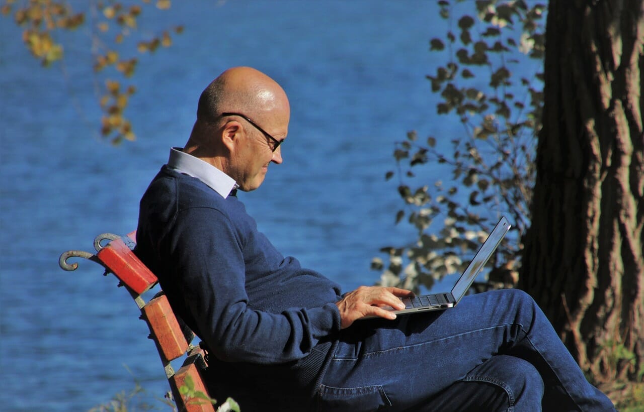 Smiling Middle-Aged Expat with Laptop in Park - English-Speaking Services for Communication