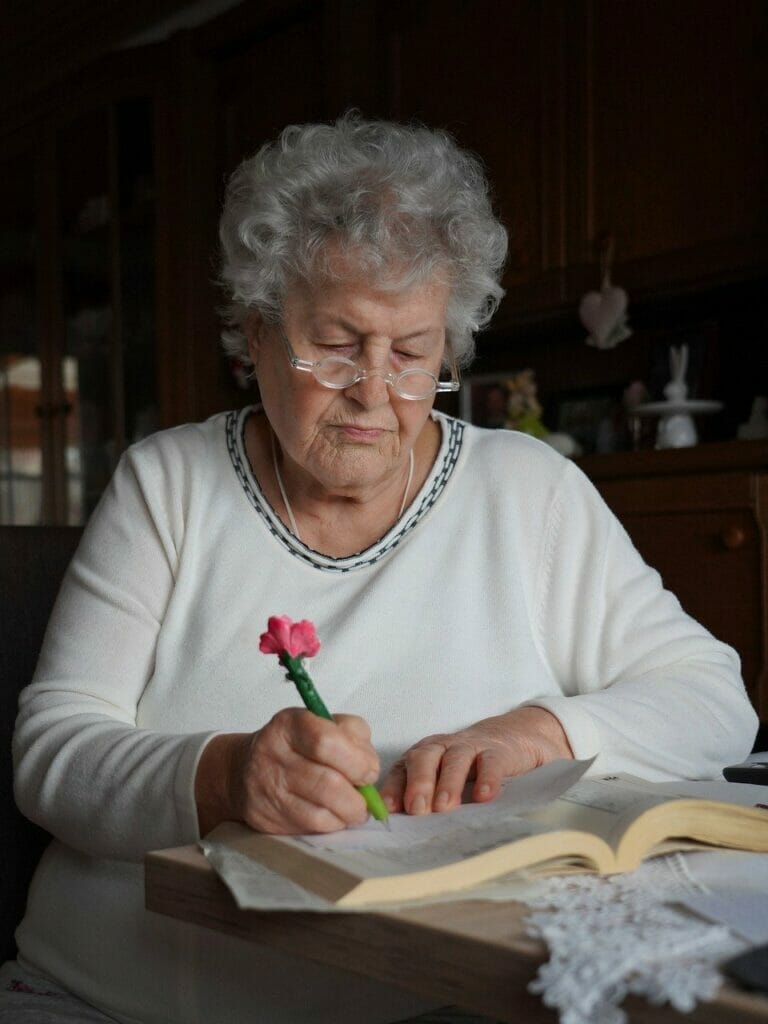 Focused Elderly Lady Writing at Table, Navigating German Pension Requirements with Professional Assistance